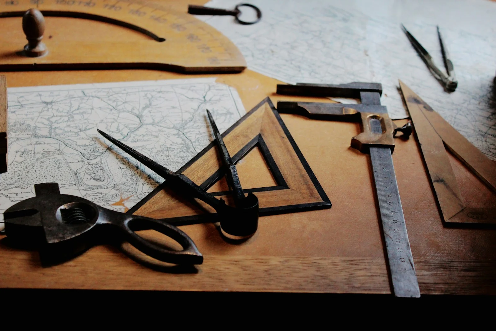 Drafting instruments and hand tools laid out on a warm wooden work table.